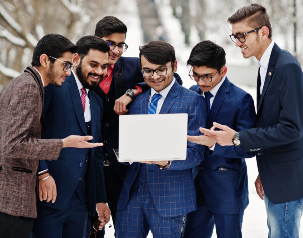 Group of six indian businessman in suits posed outdoor in winter day at Europe, looking on laptop.